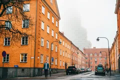 Gata med orange byggnader i Stockholm, dimmigt väder, personer och bilar på vägen.