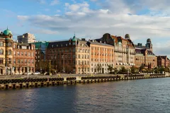 Historiska byggnader vid vattnet i Malmö, Sverige, med blå himmel och moln.